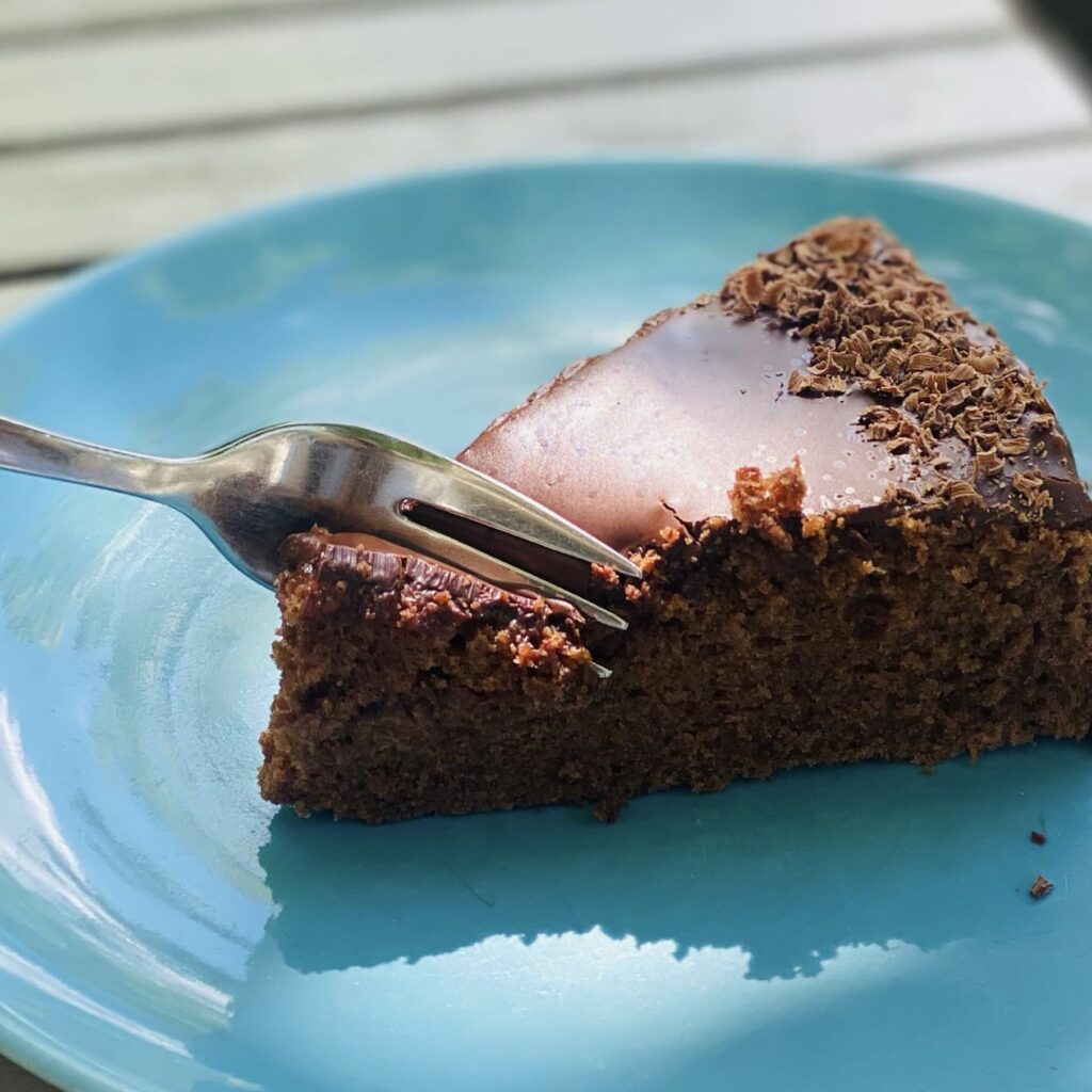 A portion of vegan sachertorte, austian chocolate cake on a turquoise plate being cut with a fork.