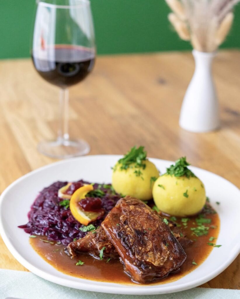 Vegan Austrian dish with  red cabbage, potato dumplings on a wooden table with a wine glass and a flower pot in the background.