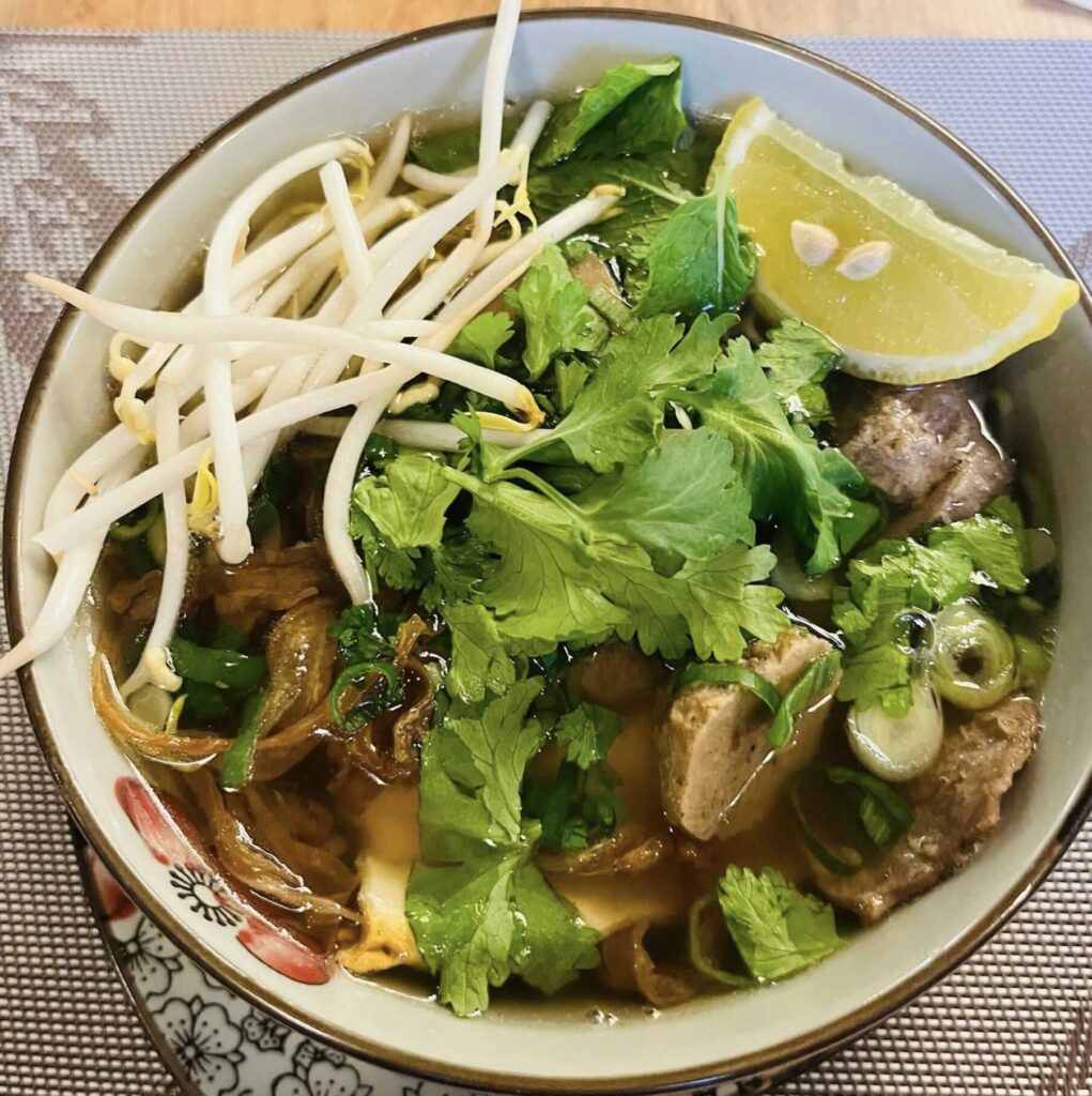 Vegan Pho garnished with a lemon slice, parsley and bean sprouts