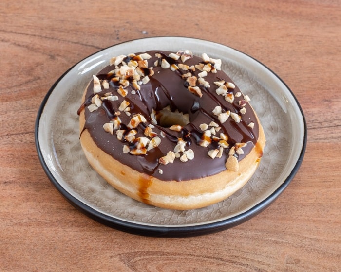 a yeasted round ring vegan donut topped with chocolate and chooped nuts on a white plate at boogie donuts in munich
