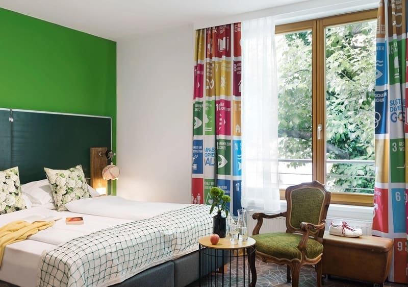 inside of an eclectic guestroom with colorful drapes and bedding at the vegan friendly hotels boutique stadthalle in vienna 