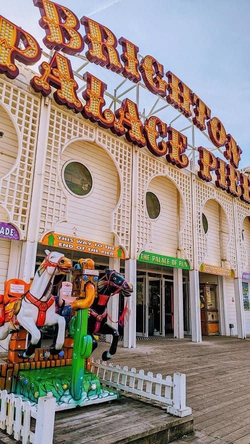 entrance to the brighton pier with the name in bright neon lettered lights and a small carousel horse