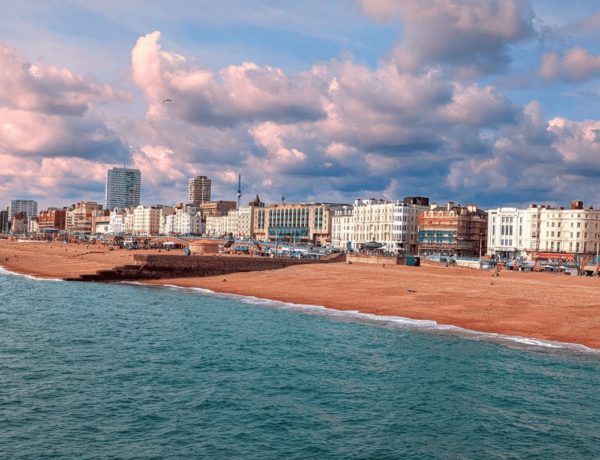 the brighton seafront with large fluffy white and pink clouds, light brown sand and stone beach and the city in the background
