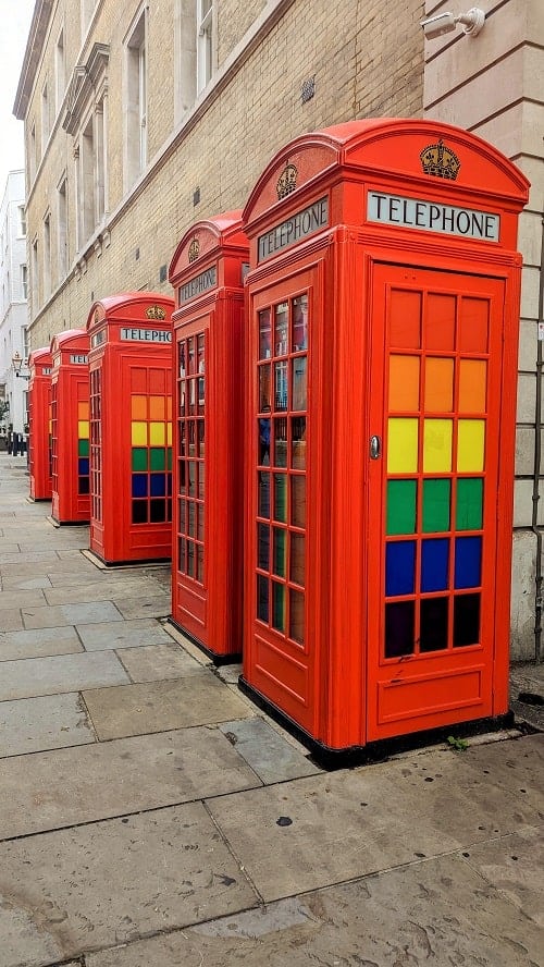 a lineup of red london telephone booths with rainbow colored glass panels