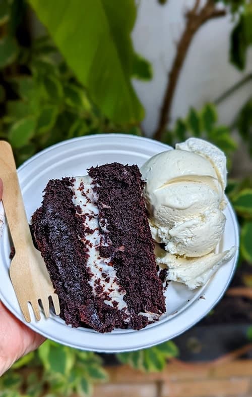 a slice of vegan and gluten free chocolate cake with cream, jam, and a large scoop of vanilla ice cream on a white plate at cookies and scream