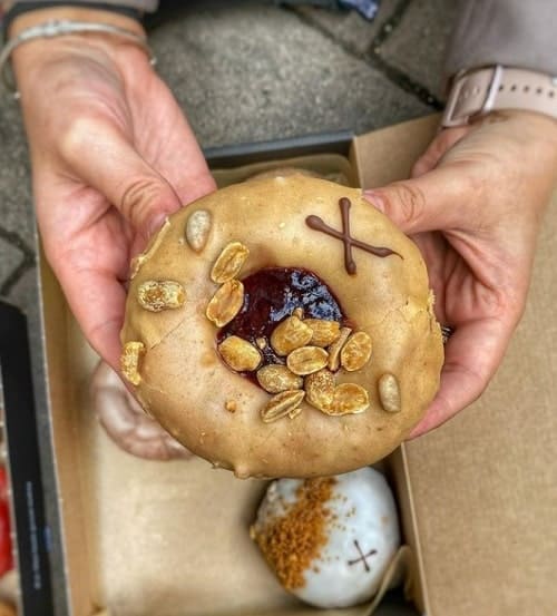 one vegan peanut butter and berry donut held with two hand above a donut box in london