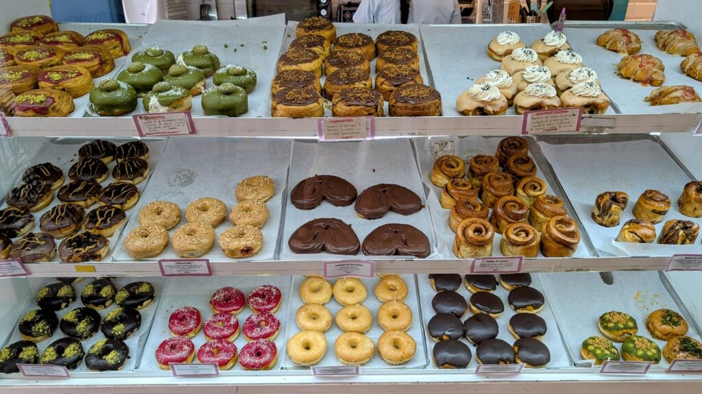 a large donut case filled with colorful vegan donuts topped with chocolate, frosting and cream at delish donuts in madrid