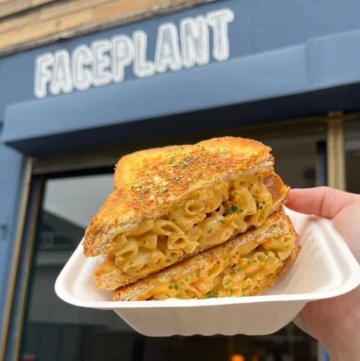 a vegan grilled mac and cheese sandwich held in front of the black face plant storefront in edinburgh
