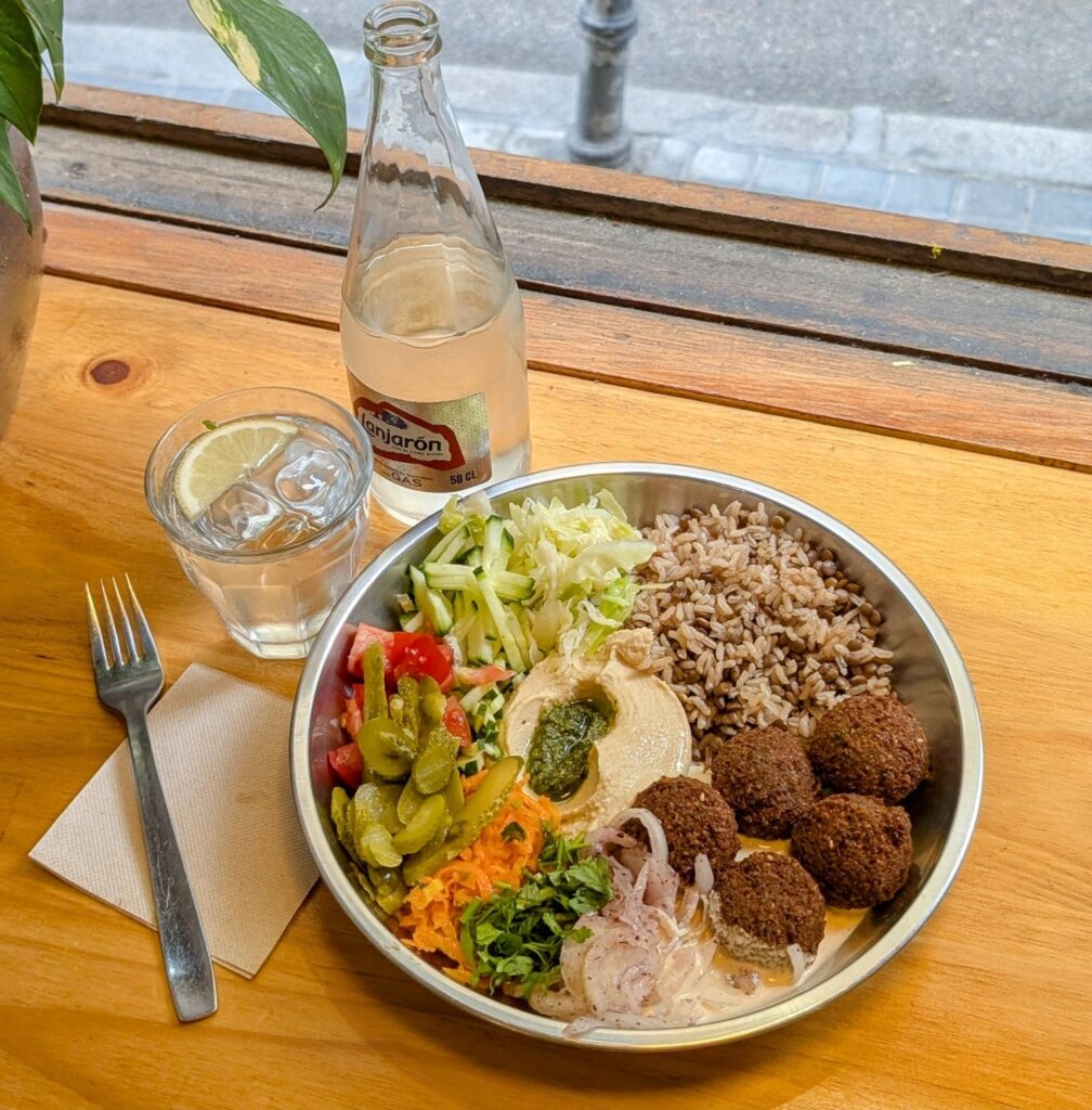 vegan falafel bowl with salad and hummus on a light wood table with a glass of water in madrid