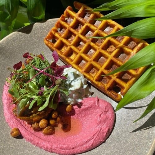 one golden vegan waffle next to a large pool of hot pink hummus in london