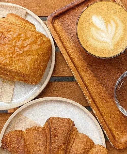 two golden vegan pastries next to a coffee with a leaf milk design on top in london