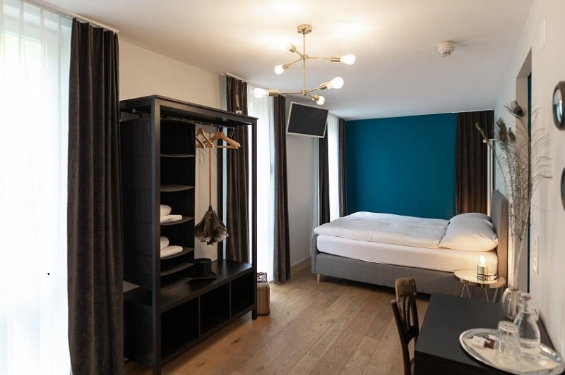 small guestroom with light flooring, one blue wall and dark furniture at the hotel landhaus in bern
