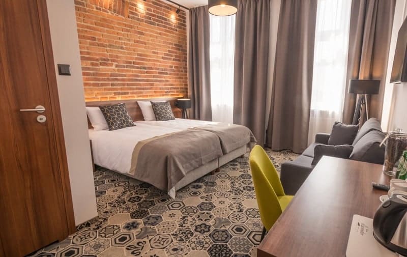 warm and welcoming guestroom with a exposed brick wall behind a double bed with white linen and a gray blanket at the hotel lavender in krakow