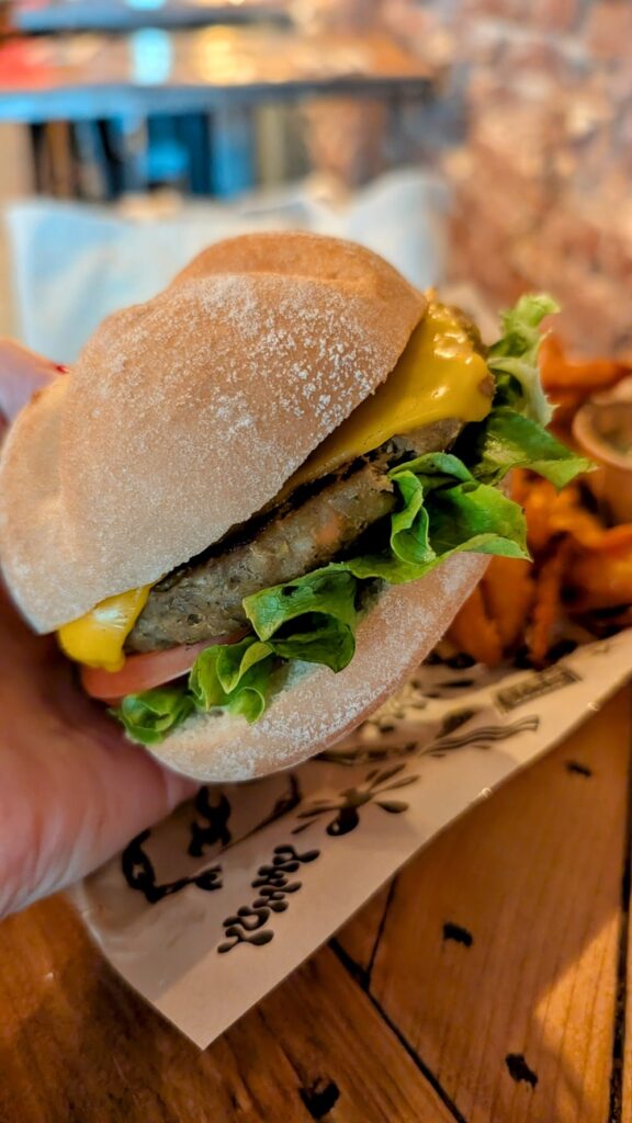 vegan and gluten free cheeseburger with lettuce held in front of a tray of sweet potato fries at mad mad vegan in madrid