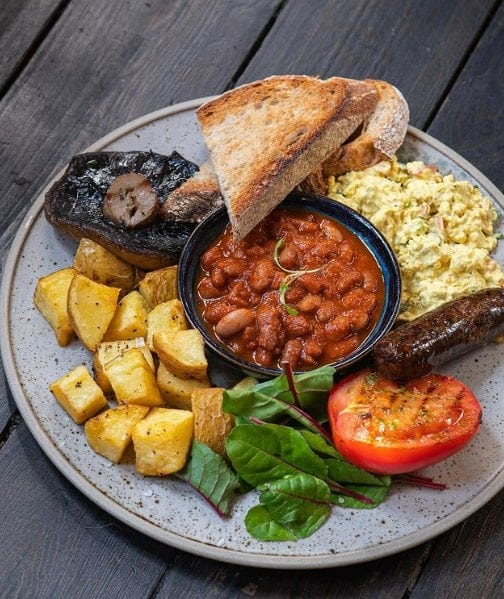 a large gray plate with a full vegan english breakfast which includes roasted veggies, tofu scramble, toast and sausage in london