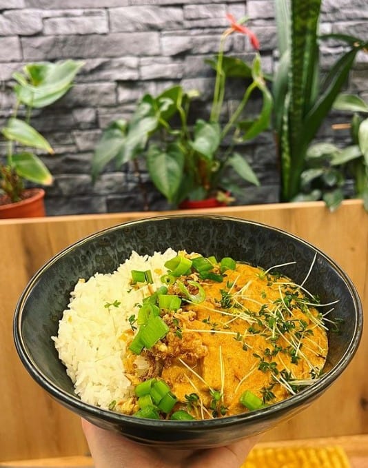 a large black bowl on a wood table filled half with white rice and the other half with a vegan yellow curry in prague