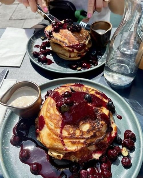 two plates in front of each other with stacks of golden vegan pancakes covered in dark berry compote in london