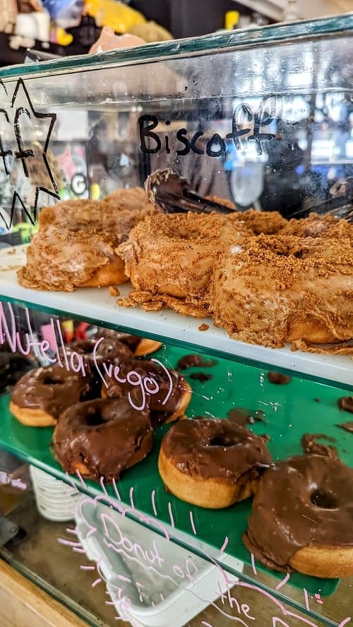 dessert case filled with ros of vegan donuts topped with chocolate, peanut butter, and nuts in brighton