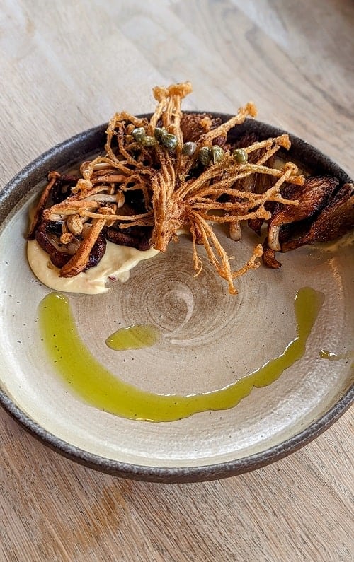 vegan crispy fried mushrooms sitting off to one side on a beige plate with a cirelc of olive oil in brighton