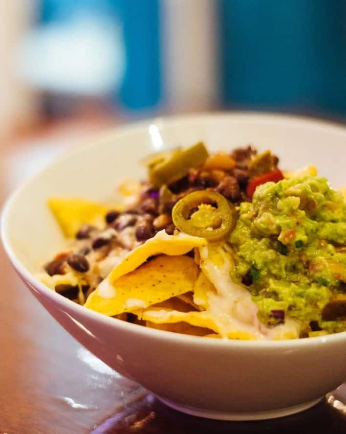 a bowl of vegan nachos covered in cheese, guacamole, beans, and jalapenos in madrid