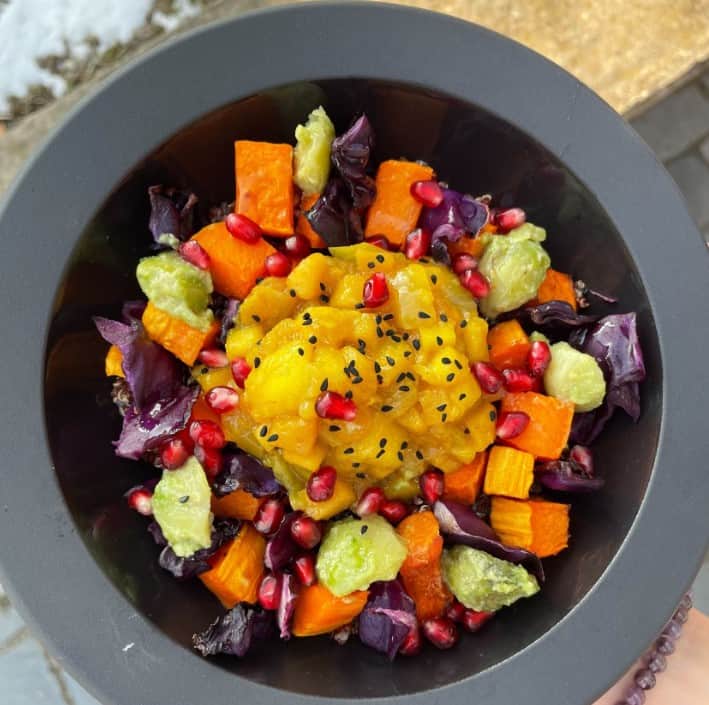 a colorful vegan salad with chunks of carrot, cabbage, and cucumber in a black bowl at planteen in budapest