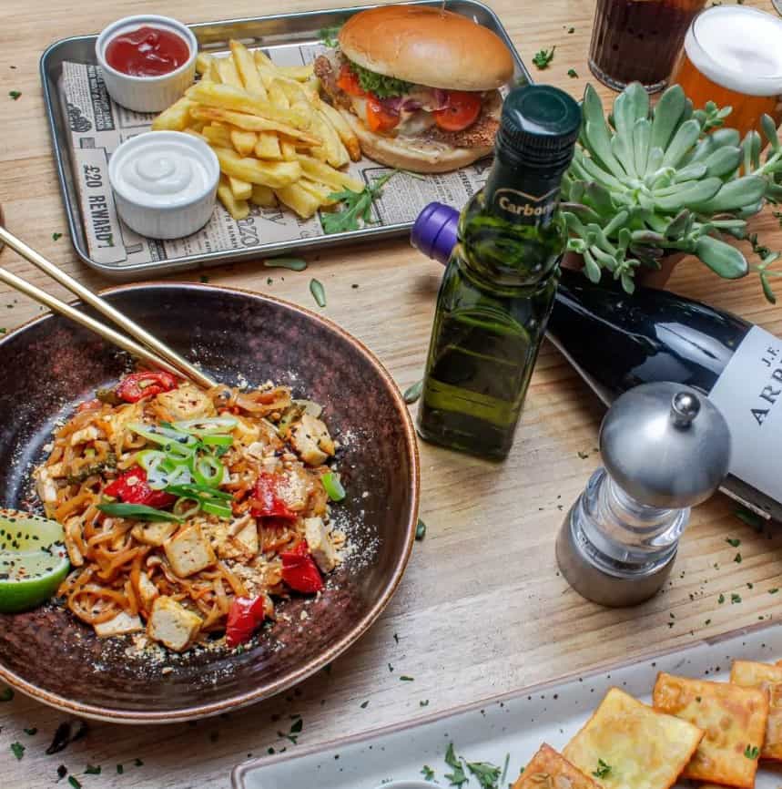 a bowl of vegan pad thai with chop sticks off to the side next to a vegan burger and a little plant at punto vegano in madrid