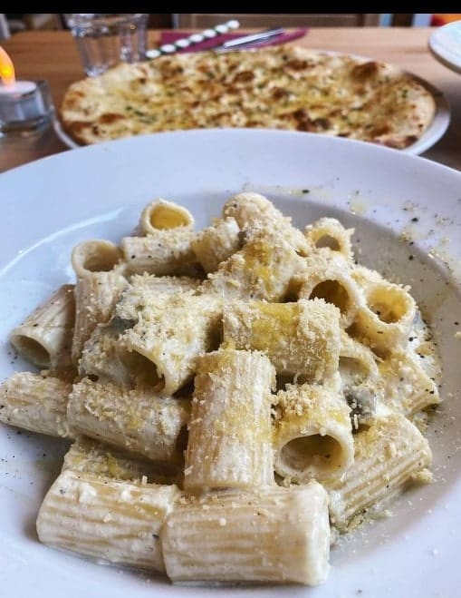 large white bowl of white vegan cream pasta with a pizza in the background in edinburgh