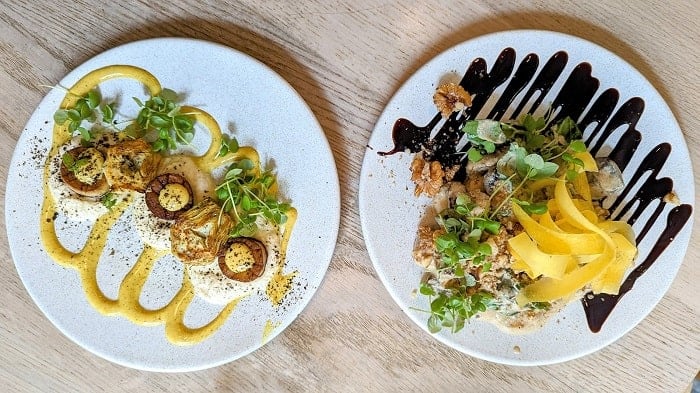 two white plates side by side with vegan mushroom scallops covered in a yellow cream and gnocchi covered in a balsamic glaze at stem and glory in london