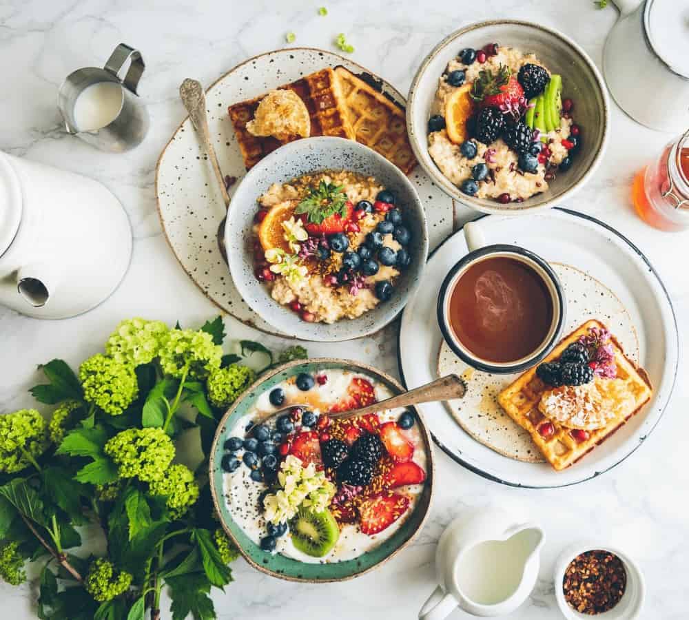 giant vegan breakfast spread with plates filled with waffles and toast and bowls filled with fruit and yogurt