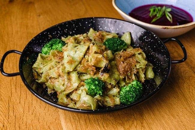 colorful vegan pasta dish with green broccoli in a black pan on a wood table in budapest