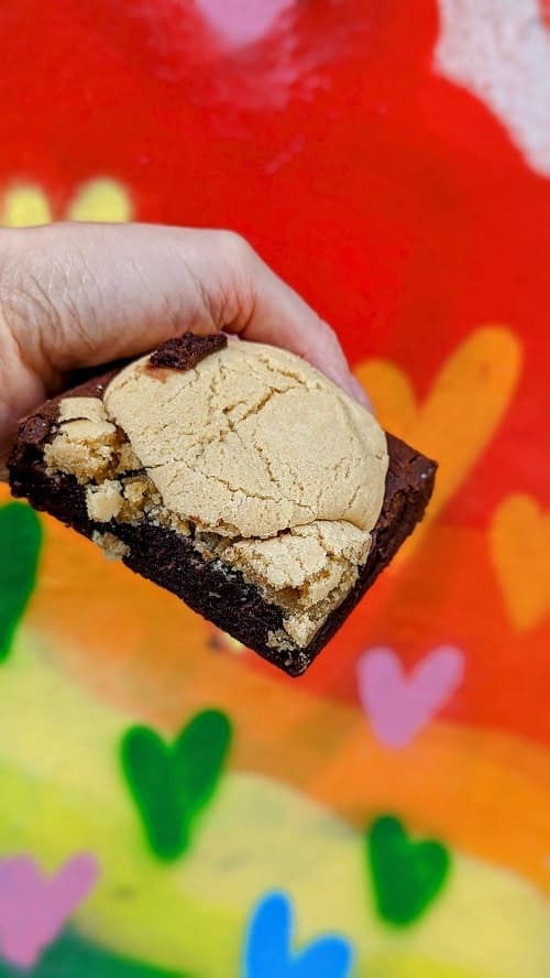vegan and gluten free chocolate brownie topped with a large mound of cookie dough infront of a brightly colored heart mural in brighton