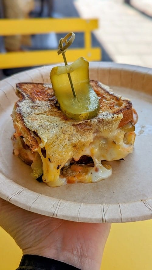vegan and gluten free grilled cheese with melted cheese coming off of the sides of the golden bread and topped with a pickle in brighton