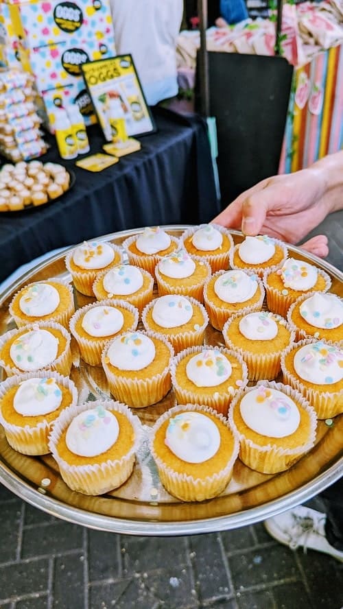 silver tray being held by someone filled with mini vegan vanilla cupcakes topped with white butter cream