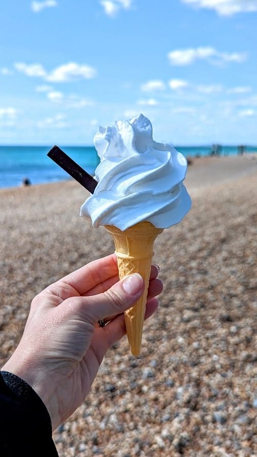 vegan mr. whippy vanilla softserve ice cream cone held in front of the brighton seafront