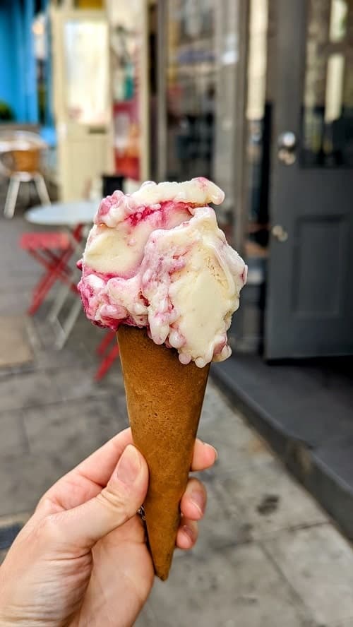 ice cream hold with one large scoop of sour cherry ice cream which is a vanilla with swirls of pink berry held on a street in brighton