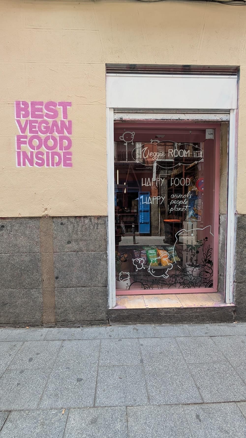 the outside of the vegan market veggie room in madrid. On the cream wall there is a pink spray pain sign that says best vegan food here
