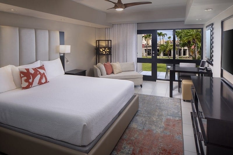 inside of a modern guest suite with white linen covered bed, large back sliding doors and light walls at Bucuti and tara beach resort in aruba