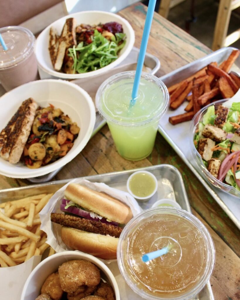 Fast Food trays over wooden plank table. Lemonades and Milkshake, burger, fries, sweet potato fries and salad.