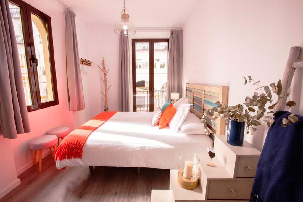 bright guest room with light colored walls and bedding and wood framed windows at Lukanda Mariana in seville