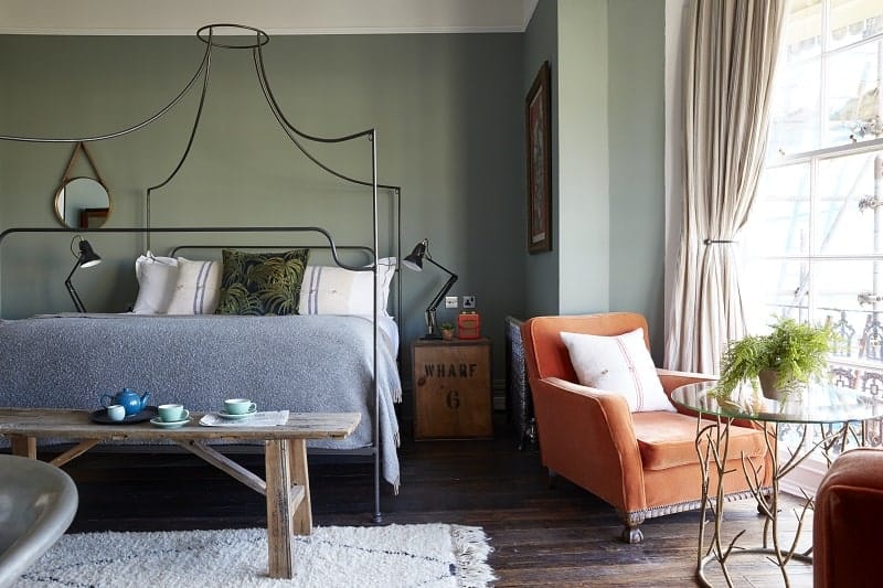 boho chic designed guestroom at the artist residence in brighton with a wire frame bed, neutral bedding and wall colors and an orange chair next to a bright window