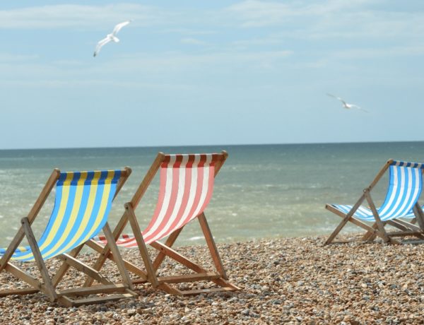 three striped cloth beach chairs sitting empty on the brighton beach with seagulls flying in the sky