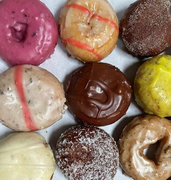 lineup of nine vegan donuts topped with chocolate, pink icing, yellow icing, coconut from the donut farm in san Francisco 