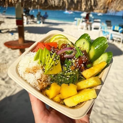 vegan poke bowl with rice, cucumber, mango, and over veggies held on the beach in aruba