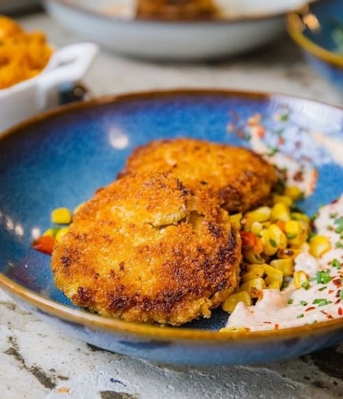 large blue bowl filled with two golden brown and crispy vegan crab cakes on a bed of corn salad in philadelphia