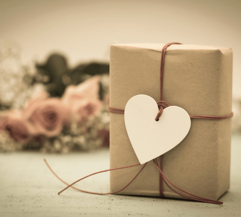 a small brown paper package wrapped with brown string and a heart shaped gift tag with flowers in the background