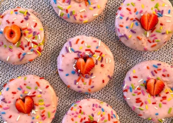7 bright pink vegan donuts topped with sprinkles and a piece of strawberry in the center from the happy vegan bakery in san Francisco 