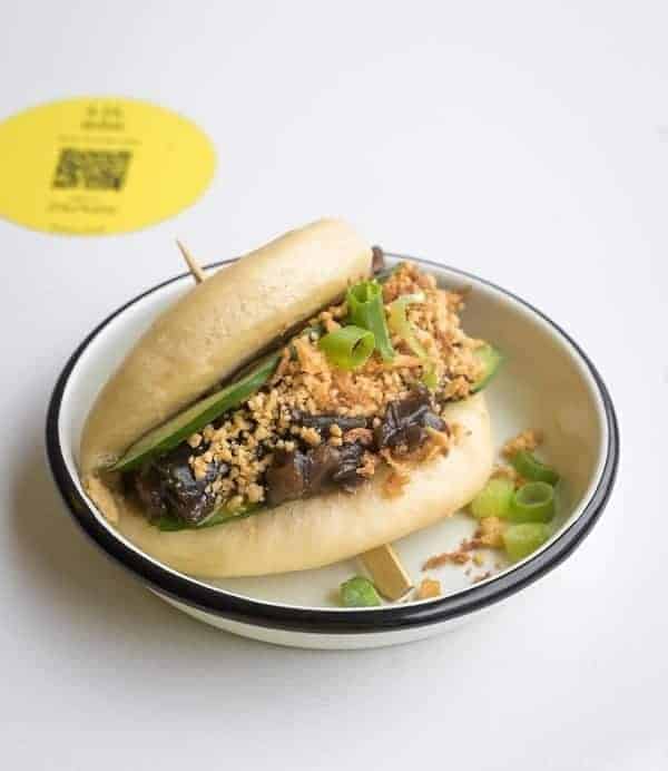 vegan bao bun stuffed with veggie meat and vegetables on a white table in brussels 
