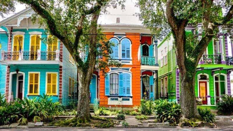 bright orange, blue, and green homes next to each other on a tree lined street in new orleans
