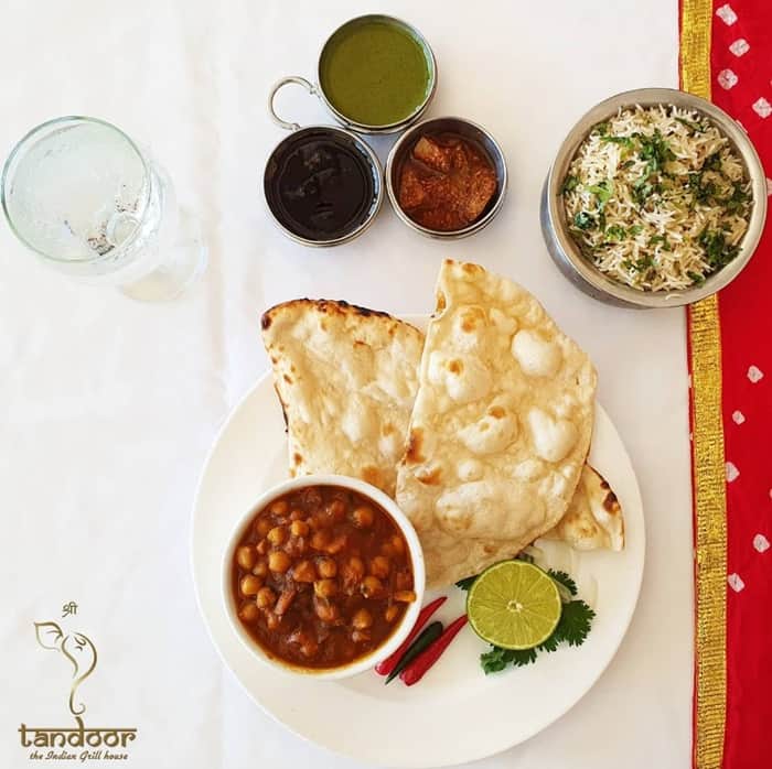 a spread of vegan indian dishes with a large white plate with a bowl of chana masala next two thin bread on a white and red tablecloth in aruba