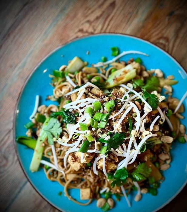 a blue bowl with vegan pad thai topped with sprouts on a wood table in warsaw